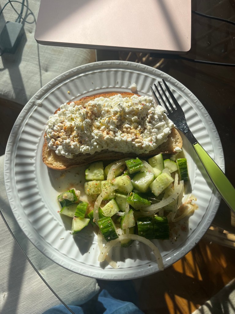A plate of food with toast topped with cottage cheese and a side of cucumbers.