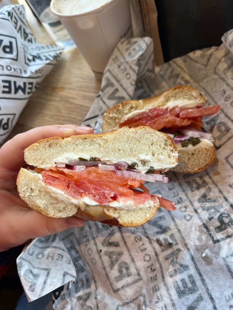A cross section of a bagel sandwich with layers of smoked salmon, tomato, onion, and cream cheese.