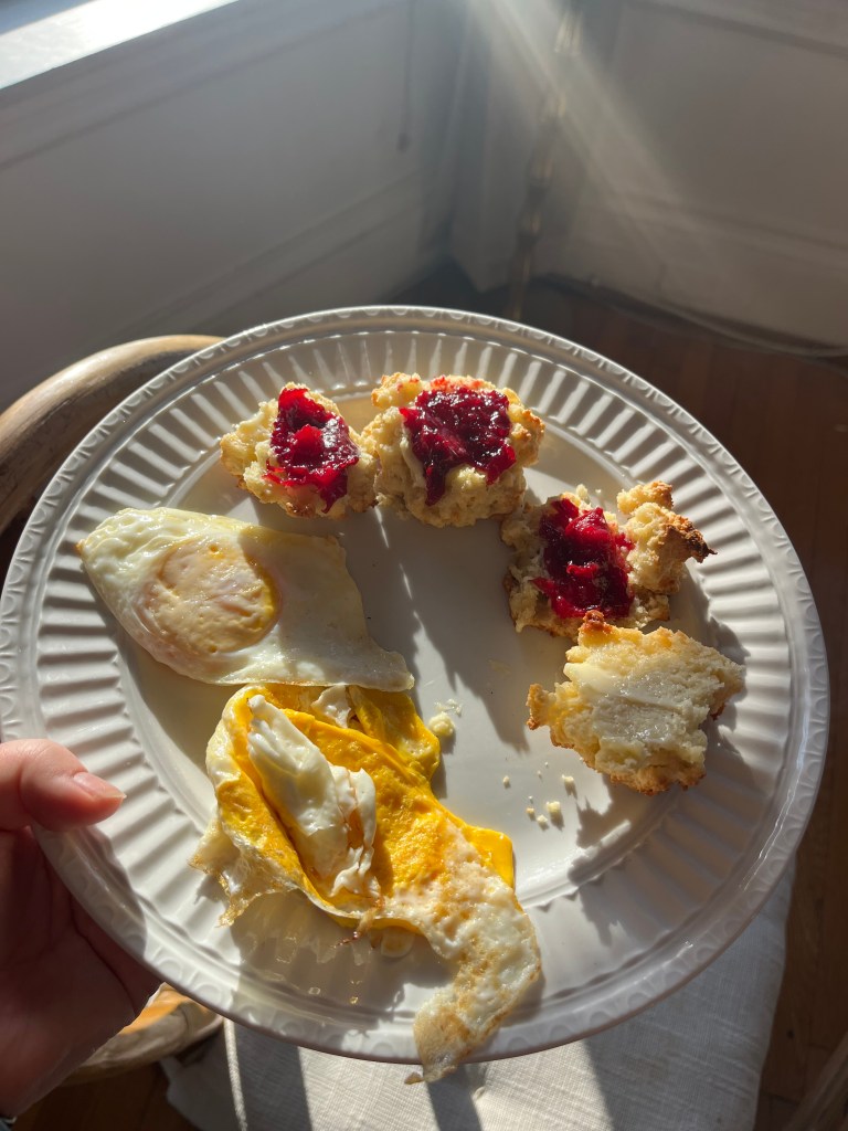 A white plate with two fried eggs and biscuits topped with jam.