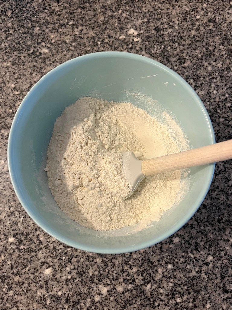 A blue mixing bowl with flour and a spatula in it.