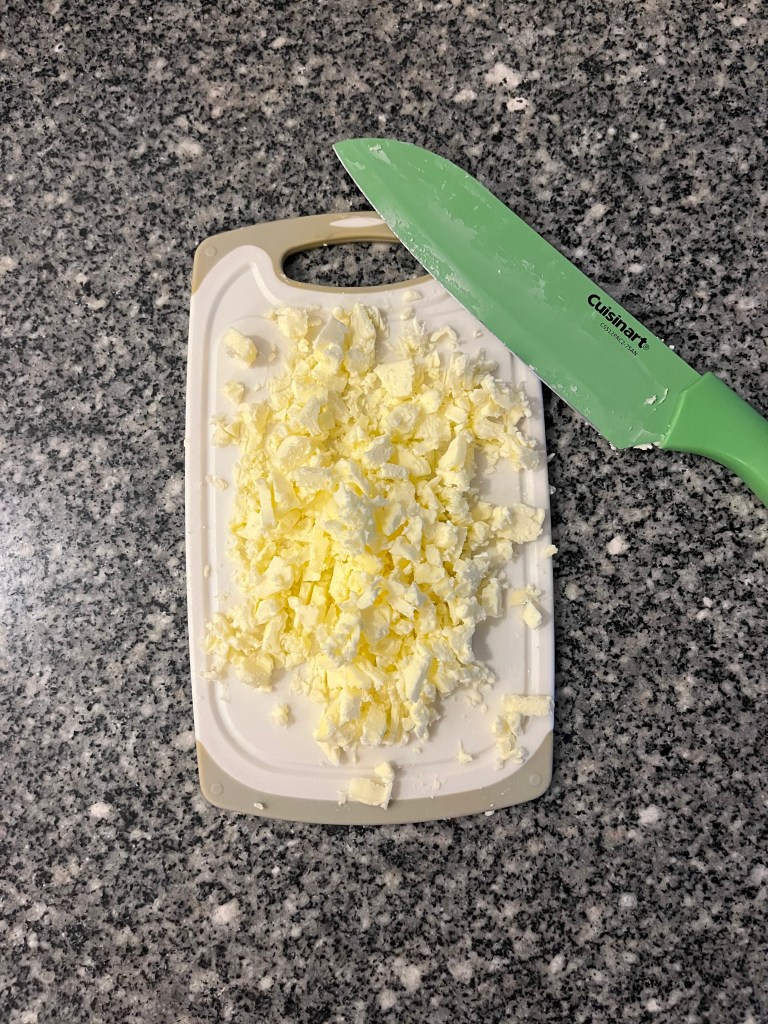 A small cutting board with chopped butter and a green knife. 