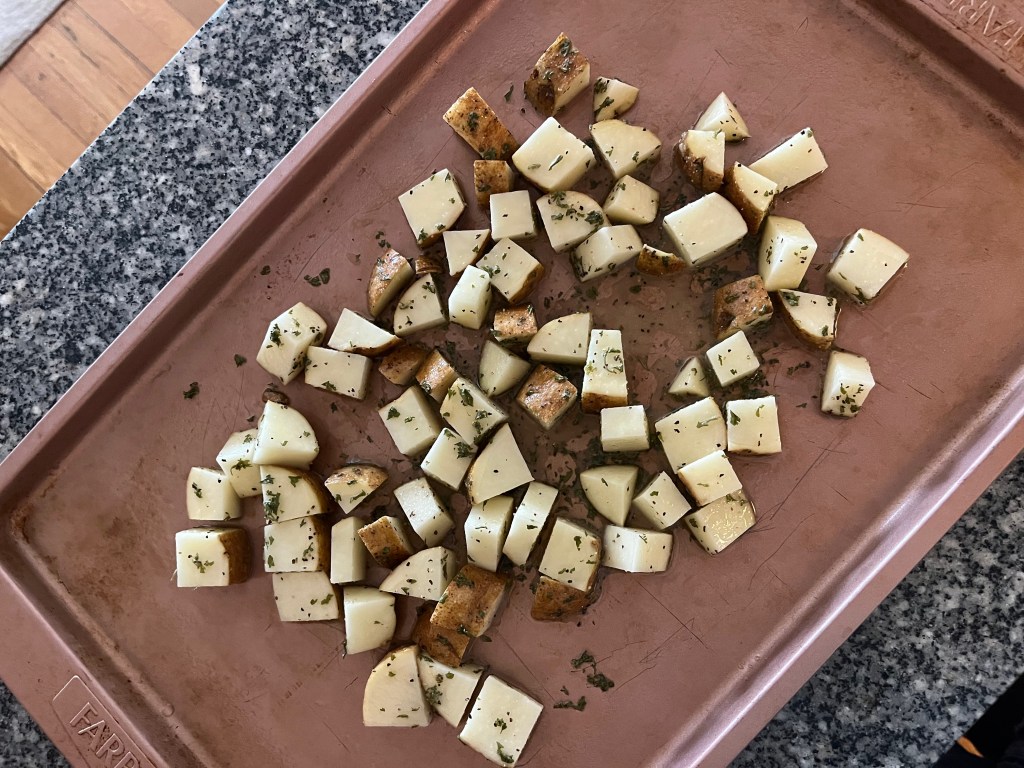 A pink baking tray with seasoned chopped potatoes.
